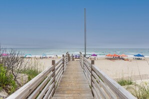 Une promenade en bois menant à une plage où l’on trouve des parasols et des chaises de plage.