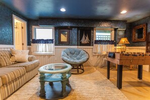 Ein gemütliches Wohnzimmer mit einer Couch, einem Sessel, einem Glastisch und einem Kicker.