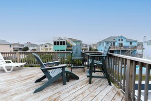 Une terrasse en bois, agrémentée de chaises et d’une table, qui offre une vue sur un quartier résidentiel avec ses maisons.