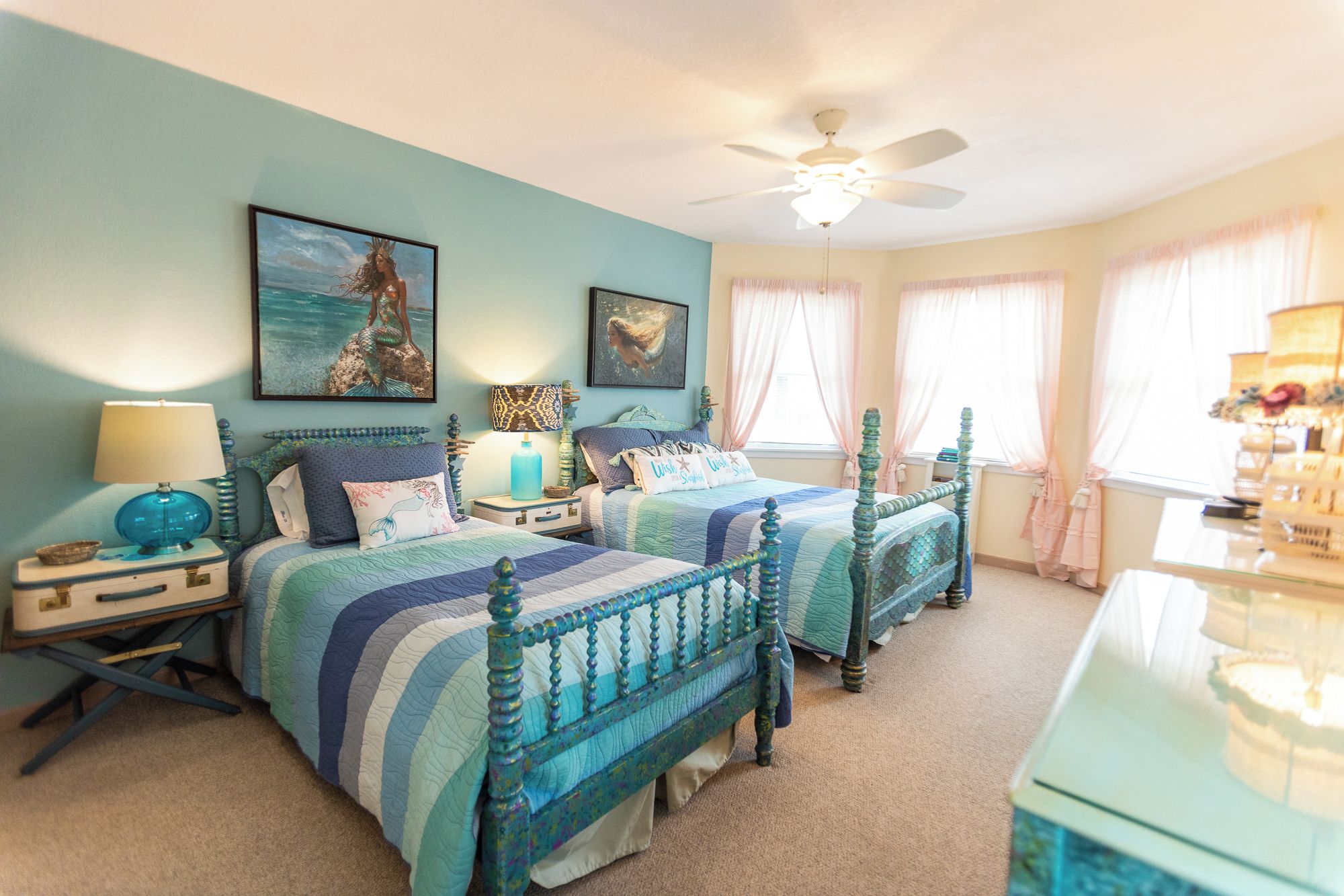 A bedroom with two beds, a ceiling fan, and artwork on the walls.