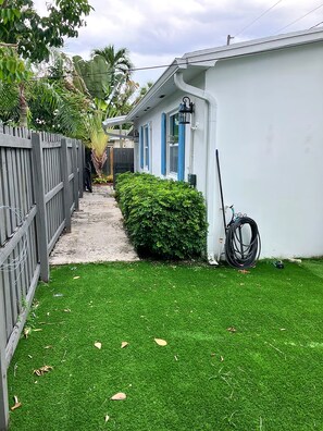 En bostadsfastighet med en stenlagd gång som leder till en vit byggnad med blå detaljer, ett inhägnat område och en välskött gräsmatta.