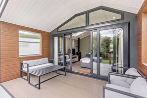 A modern interior with a wooden wall, a bench, a sofa, and a glass door leading to an outdoor area. - Prion 1.0 Pet (Denbigh)