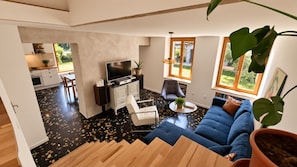 A modern living room with a blue sofa, a white coffee table, and a TV stand. There is a staircase leading to another level, and a kitchen area is visible in the background. - Lovely 3-bedroom farmhouse in Les Avenières - 1 min from Walibi & Horse Friendly (Les Avenières Veyrins-Thuellin)