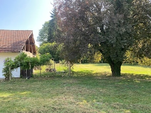 Un bâtiment rustique, doté d’un toit en tuiles, entouré d’une pelouse et d’un grand arbre.