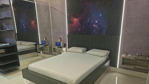 Ein modernes Schlafzimmer mit einem großen Bett, einem Nachttisch, einem an der Wand montierten Fernseher und einer Wand mit Galaxie-Motiv.