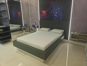 A modern bedroom with a large bed, a nightstand, a wall-mounted TV, and a galaxy-themed wall. - Luxus Motel (Tucano)