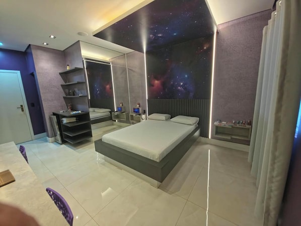 A modern bedroom with a large bed, built-in shelving, a galaxy-themed wall, and a minimalist design. - Luxus Motel (Tucano)