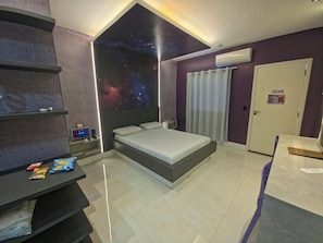 A bedroom with a bed, a nightstand, a shelf with snacks, a wall-mounted air conditioner, and a door.