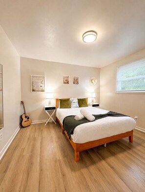 A bedroom with a wooden bed, a guitar, a nightstand, and a wall-mounted light fixture. - Southern Serenity - Cozy 2 BR • Near Nashville (La Vergne)