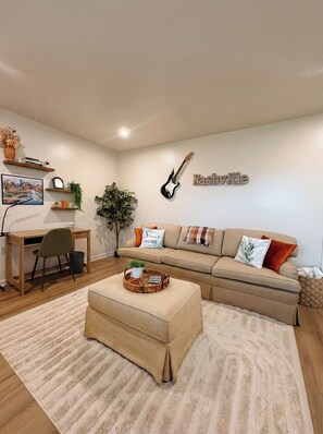 A modern living room with a sofa, coffee table, and a guitar on the wall. - Southern Serenity - Cozy 2 BR • Near Nashville (La Vergne)