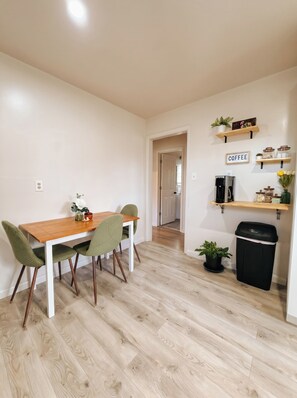 A dining area with a wooden table and chairs, a coffee station, and a trash bin. - Southern Serenity - Cozy 2 BR • Near Nashville (La Vergne)