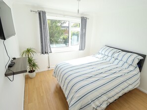 A bedroom with a bed, a potted plant, a window with curtains, and a mounted television. - Mariner's Nook (Cleethorpes)