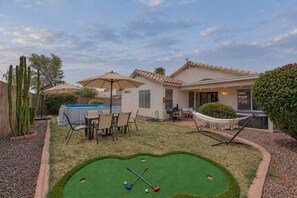 A residential property with a swimming pool, a patio with outdoor furniture, a small putting green, and a hammock.