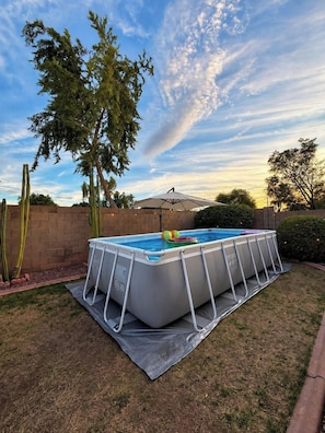An above-ground swimming pool with a ladder, surrounded by a grassy area and a brick wall. - Pool, Tub & Mini Golf |SF Stadium, Westgate, more (Glendale)
