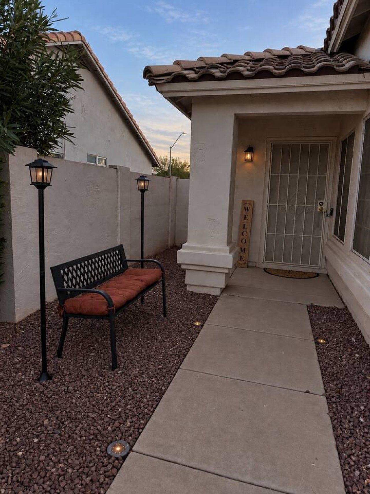 A patio area with a bench, a pathway, and a door with a welcome sign.