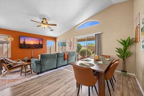 A modern living room with a sofa, dining table, chairs, a ceiling fan, and artwork on the walls.
