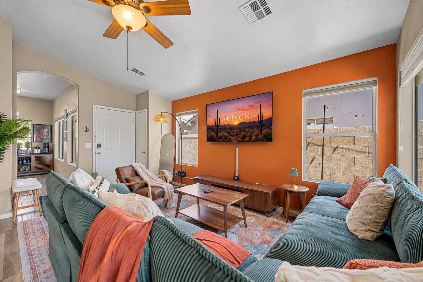 A living room with a large sofa, a coffee table, a ceiling fan, and a painting of Arizona.