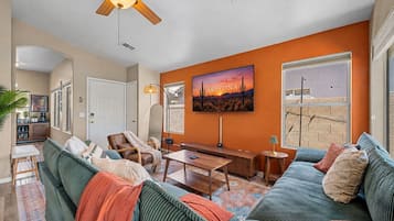 A living room with a large sofa, a coffee table, a ceiling fan, and a painting of Arizona.
