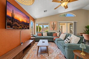 A spacious living room with a large sofa, a coffee table, and a ceiling fan.