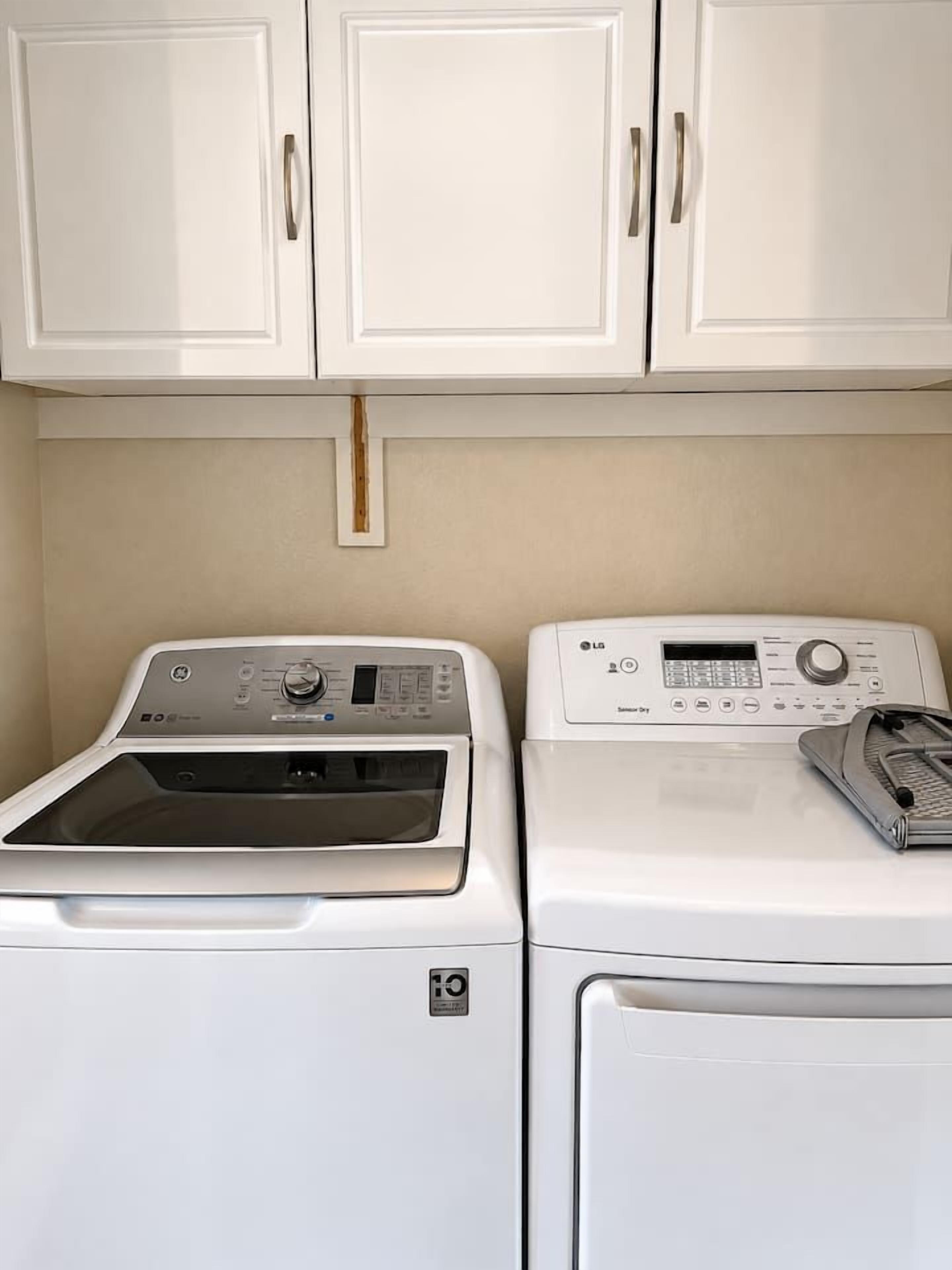 A laundry area with two white washing machines and cabinets above.