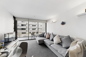 A modern living room with a grey sofa, a glass coffee table, and a flat-screen TV. - Executive 2-bed Apartment Near Kingston Hub (Canberra)