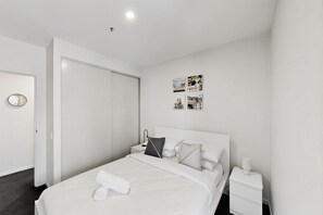 A hotel room with a bed, a bedside table, a nightstand, a wall clock, and a door. - Executive 2-bed Apartment Near Kingston Hub (Canberra)