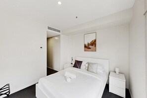Ein Hotelzimmer mit Bett, Nachttischen, einem Wandbild und einer Tür zu einem anderen Raum.