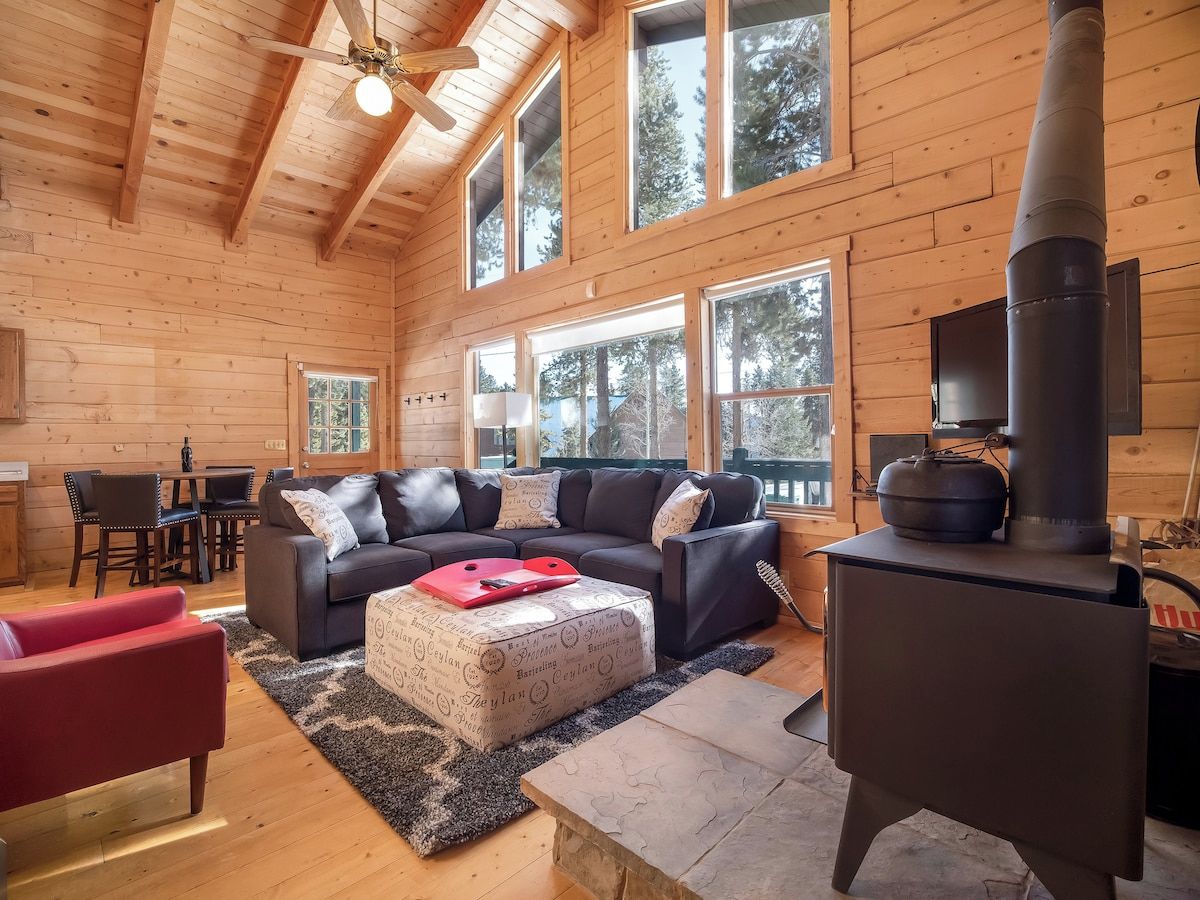 Ein Blockhaus-Interieur mit Kamin, einer Couch, einem roten Sessel und großen Fenstern.