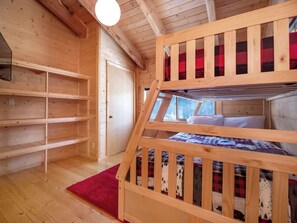 Uma cama de beliche com cobertor xadrez vermelho e preto, uma estante de madeira e um tapete vermelho sobre piso de madeira.