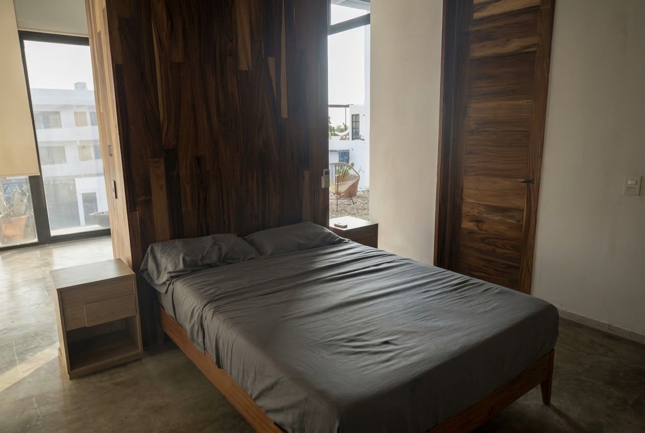 Ein modernes Schlafzimmer mit Bett, Holzwandverkleidung, einem Nachttisch und Blick ins Freie.