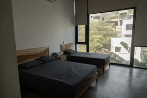 Een slaapkamer met twee bedden, een houten hoofdbord, een nachtkastje en een groot raam met uitzicht op gebouwen en bomen.