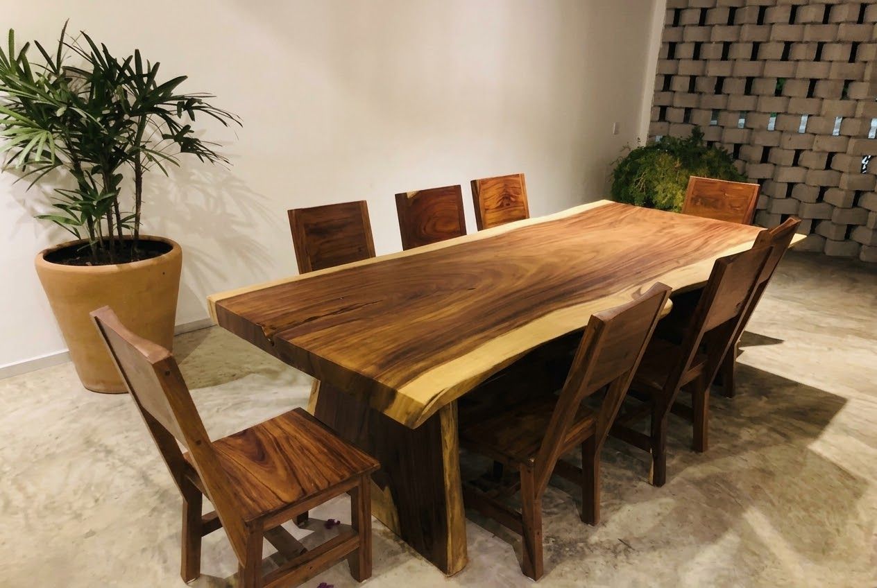 A rectangular wooden dining table with six chairs, a potted plant, and a brick wall.