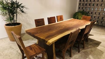 A rectangular wooden dining table with six chairs, a potted plant, and a brick wall.