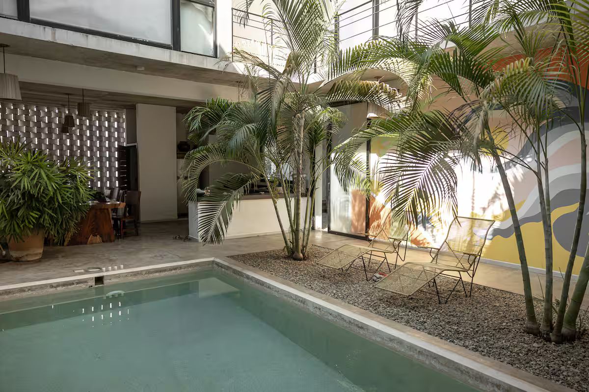 An indoor pool area with palm trees, a seating area, and a modern architectural design.