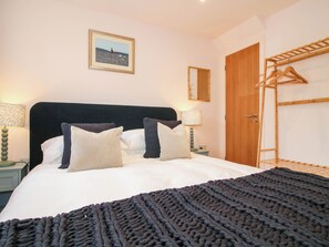 A neatly made bed with pillows and a blanket, a bedside table with a lamp, a wooden door, and a wall-mounted mirror. - Little Red Barn (Shrewsbury)