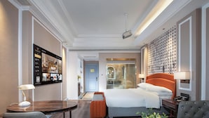 Una camera d'albergo con un letto, una scrivania, una sedia, un divano, una lampada e una televisione a parete.