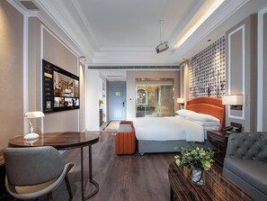 Una habitación de hotel con una cama, un escritorio, una silla, un sofá, una lámpara y un televisor montado en la pared.