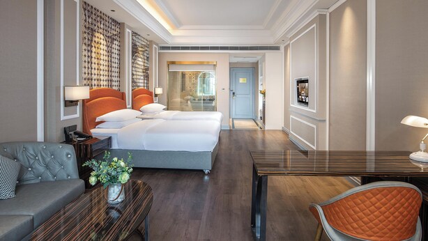 Camera d'albergo con un letto grande, un divano, una scrivania e una sedia. Si apre una porta su un balcone.