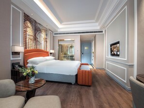 Una habitación de hotel con cama, mesita de noche, lámpara y televisor en la pared.