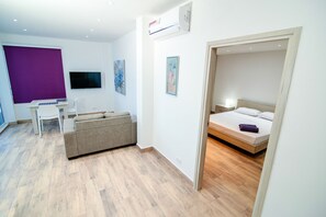 Quarto de hotel moderno com cama, escrivaninha, sofá e televisão.
