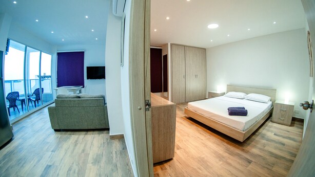 A modern hotel room with a balcony, a sofa, a bed, and a wardrobe. - Vrbo Property (Cartagena de Indias)