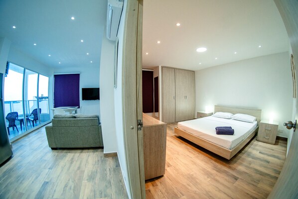 Quarto de hotel moderno com varanda, sofá, cama e guarda-roupa.