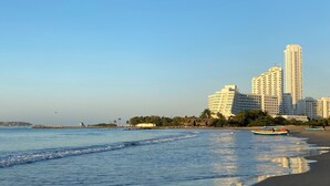 A beach with a clear sky, calm sea, and a row of tall buildings in the background. - Vrbo Property (Cartagena de Indias)