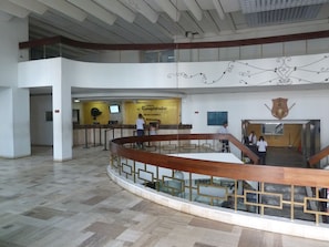 Um hall amplo com teto alto, escadaria central e área de recepção com a placa 'el Conquistador'.