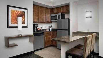 A compact kitchen with wooden cabinets, a stainless steel refrigerator, a built-in microwave, and a small dining area with a bench.