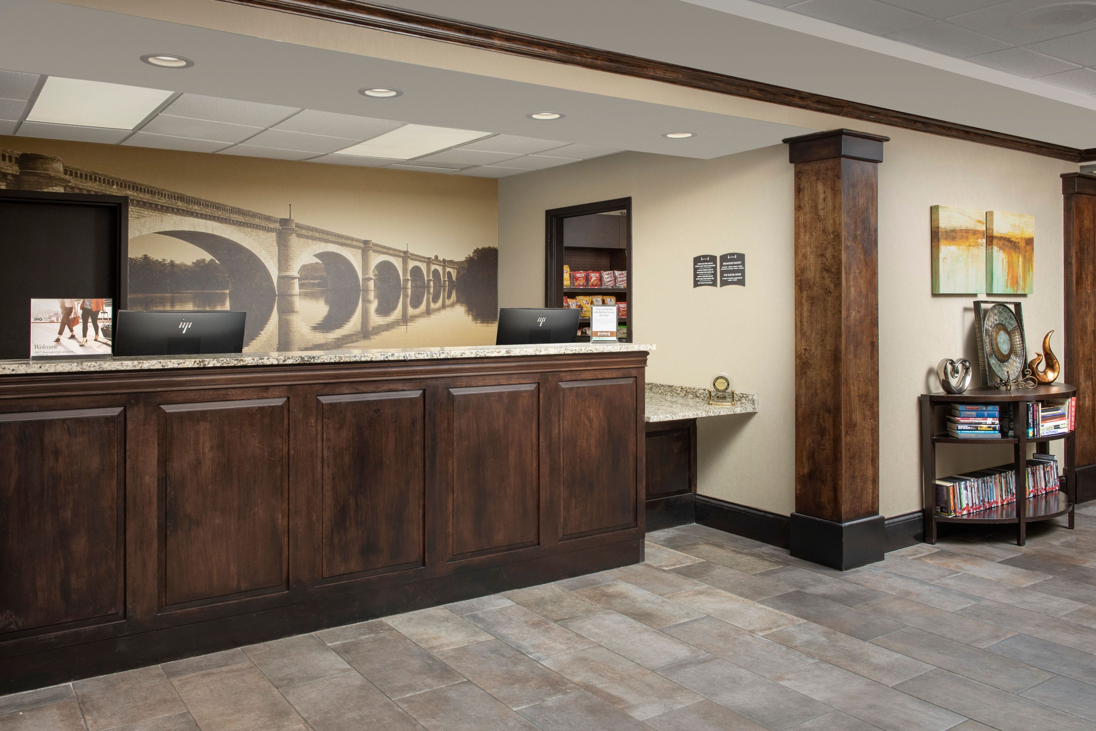 A reception area with a marble counter, wooden cabinets, a laptop, a bookshelf, and a wall mural.