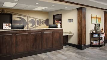 A reception area with a marble counter, wooden cabinets, a laptop, a bookshelf, and a wall mural.