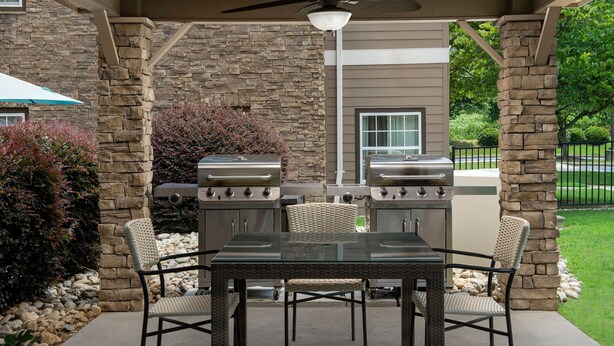 Une terrasse extérieure avec des murs en pierre, un barbecue, des chaises en osier et une table en verre.