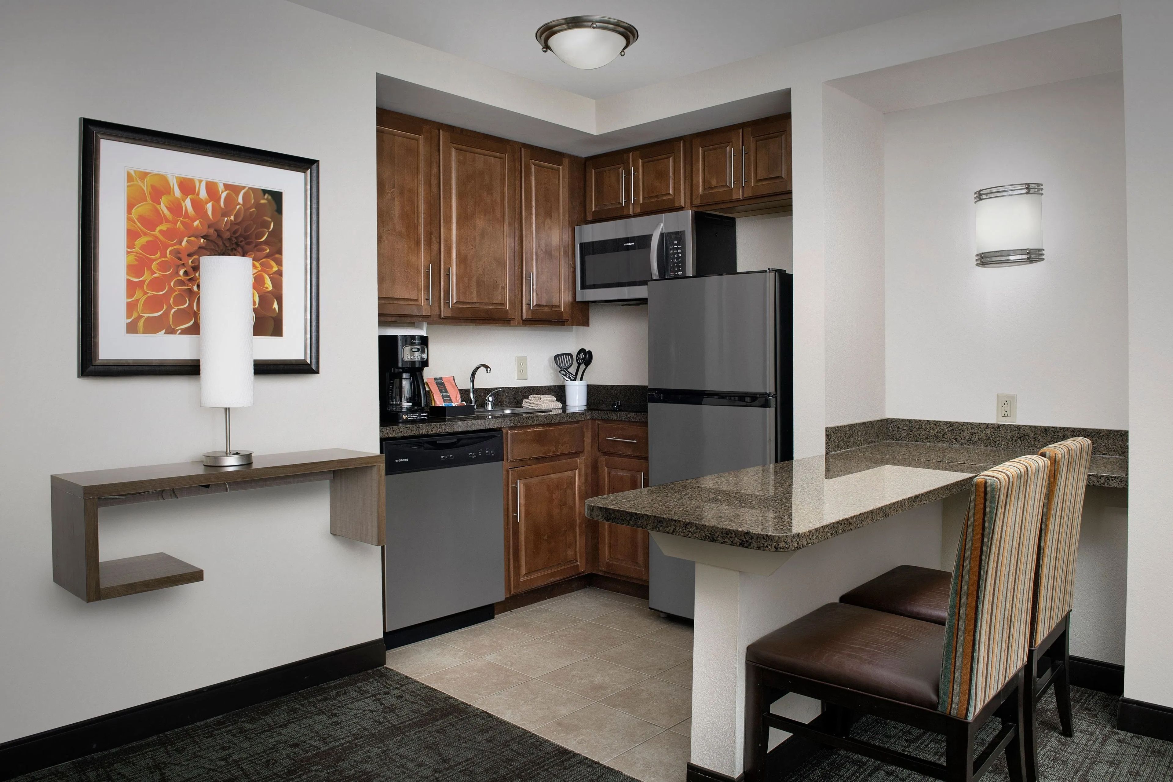 A compact kitchen with wooden cabinets, a stainless steel refrigerator, a built-in microwave, and a small dining area with a bench.