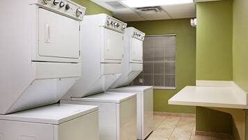 A laundry room with stacked washers and dryers, a window with blinds, and a small counter.
